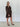 Woman wearing a brown patterned dress against a white wall