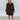 Woman wearing a brown patterned dress against a white wall.
