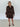 Woman wearing a brown patterned dress against a white wall.
